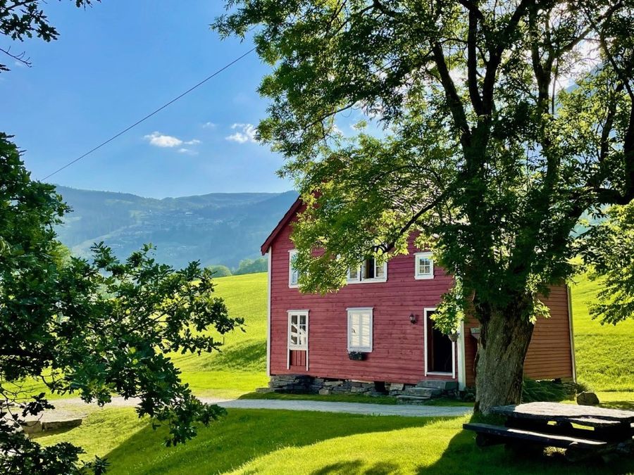 Raudt hus på tunet i sommarsol